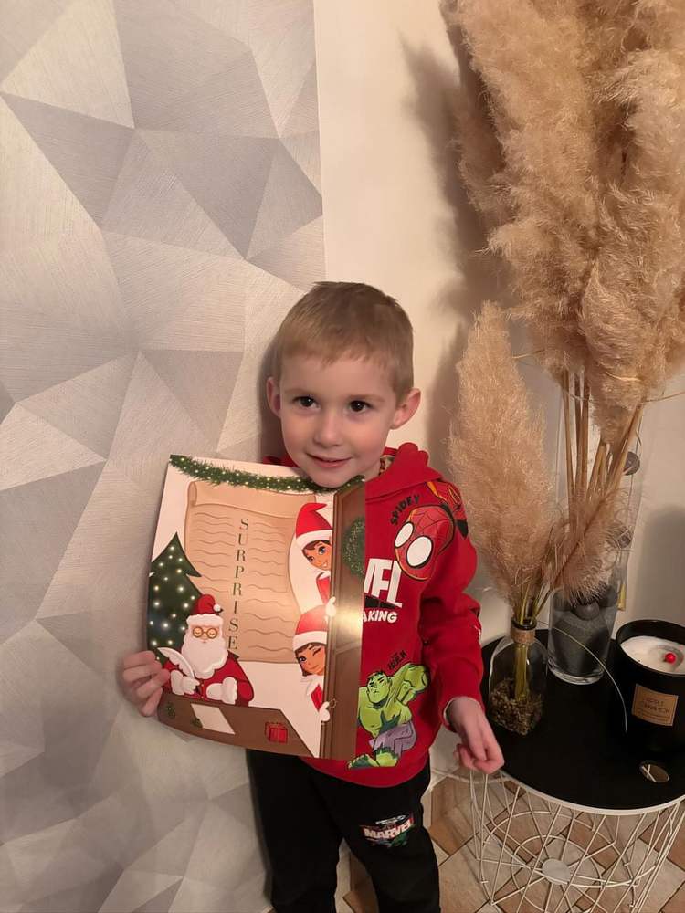 Jeune garçon souriant tenant le livre Surprise illustré du Père Noël et de deux lutins
