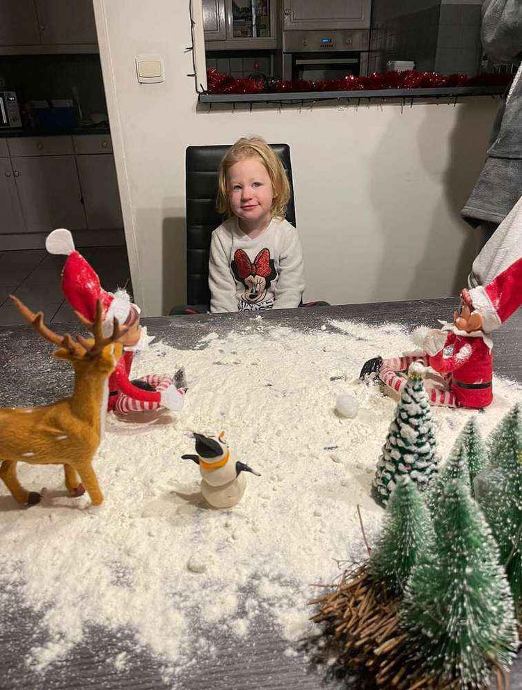 Petite fille souriante devant un paysage enneigé en farine créé sur la table par deux lutins