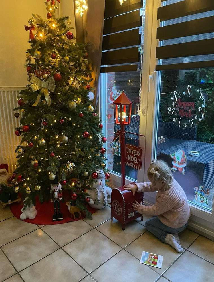 Petite fille agenouillée devant la boîte aux lettres du Père Noël, près du sapin décoré