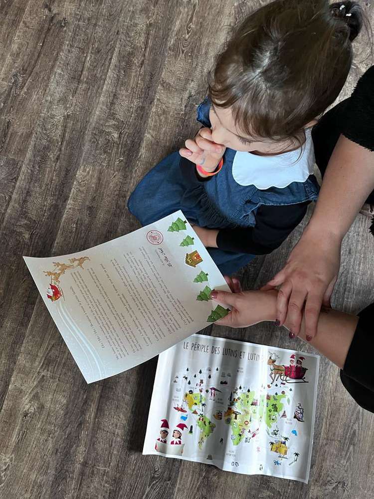Petite fille et adulte assis au sol devant une lettre du Père Noël et la carte du périple des lutins
