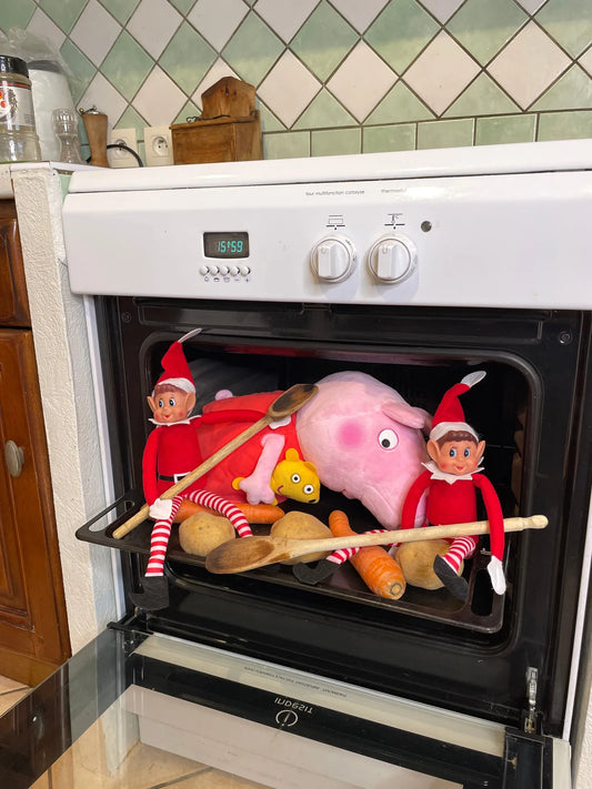 Deux lutins farceurs installés dans le four ouvert avec une peluche cochon rose, des cuillères en bois et des légumes