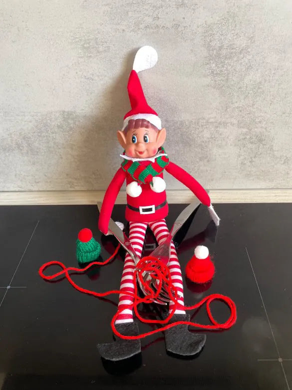 Lutin au tricot, entouré de laine rouge emmêlée et de deux petits bonnets à pompon