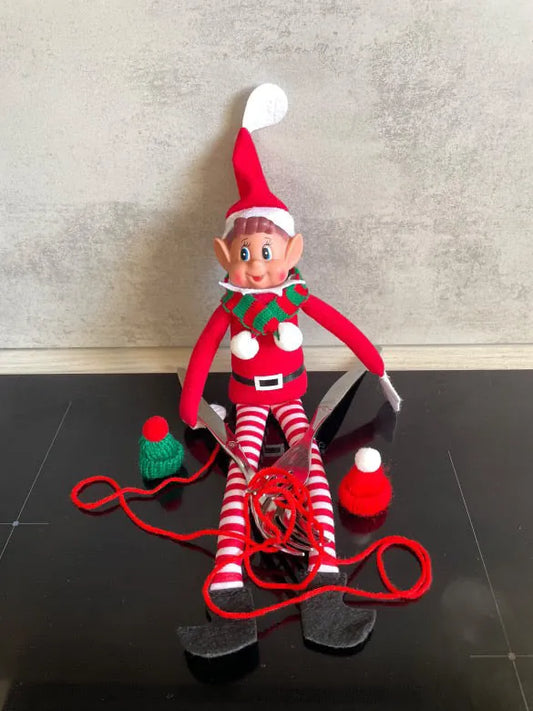 Lutin au tricot, entouré de laine rouge emmêlée et de deux petits bonnets à pompon