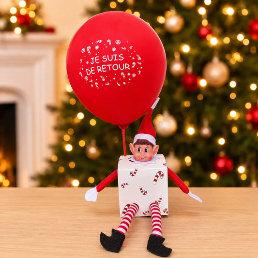 Kit d'arrivée du Lutin Farceur : le lutin assis sur sa boîte avec un ballon Je suis de retour, devant un sapin de Noël